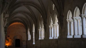 Vue perspective d'une galerie voûtée en pierre avec des arches romanes dans une abbaye historique.