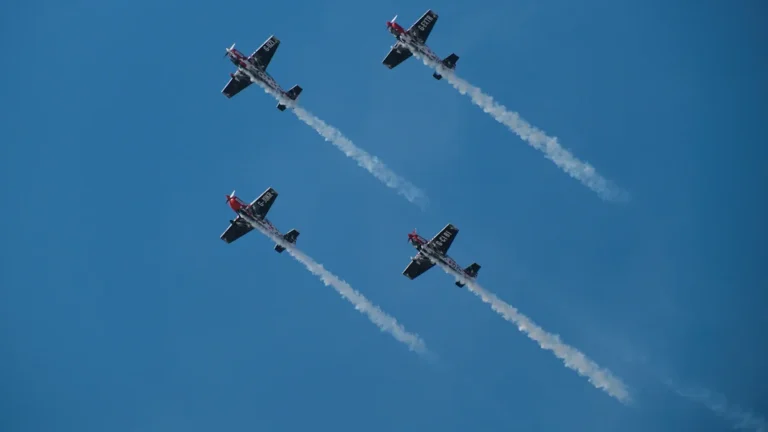 Formation de quatre avions de voltige aérienne effectuant un vol synchronisé dans un ciel bleu.