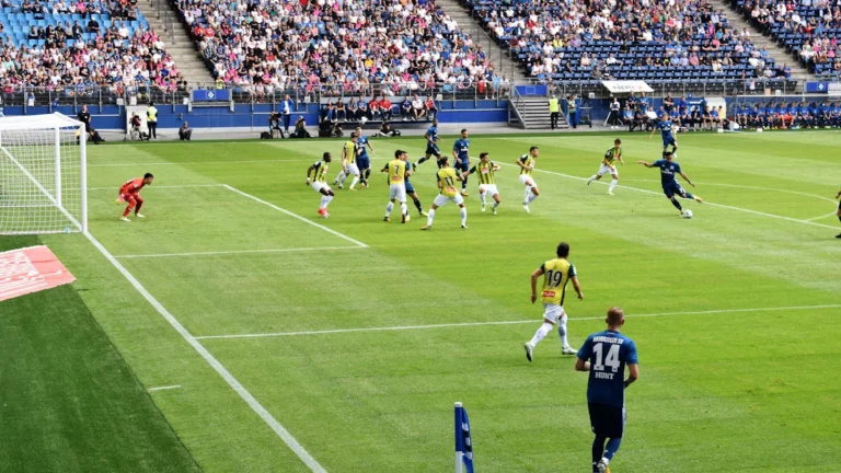 Vue d'ensemble d'un match de football disputé devant des tribunes combles dans un grand stade.