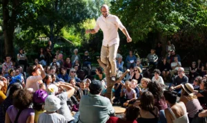Un acrobate en équilibre sur une branche devant une foule attentive dans un parc ensoleillé.