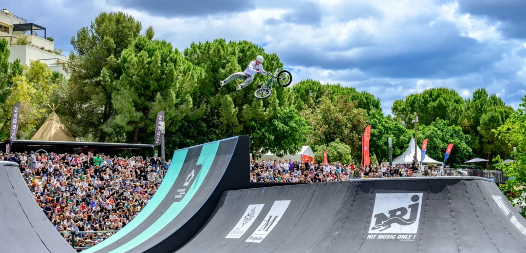 Un cycliste BMX réalise une figure aérienne au-dessus d'une rampe devant une foule dense.