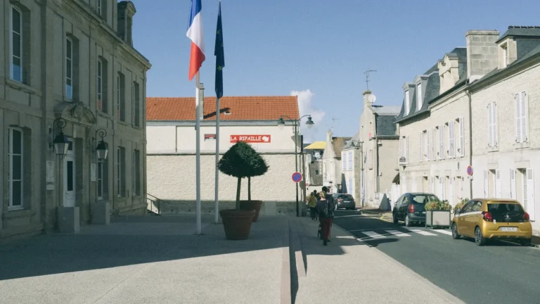 Une place publique en France avec des drapeaux français et européen devant un bâtiment municipal.