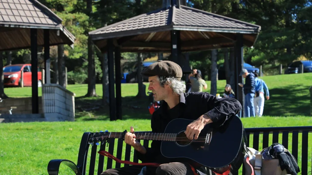 Un musicien amateur jouant de la guitare acoustique sur un banc dans un parc public à Lille.