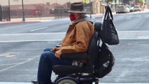 Un homme en fauteuil roulant électrique traverse une rue urbaine, illustrant les défis de l'accessibilité.