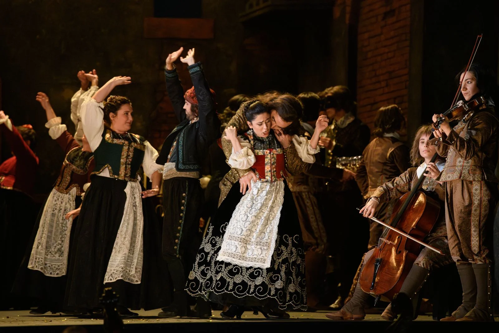 Acteurs d'opéra en costumes d'époque sur scène avec des danseurs et des musiciens d'orchestre.