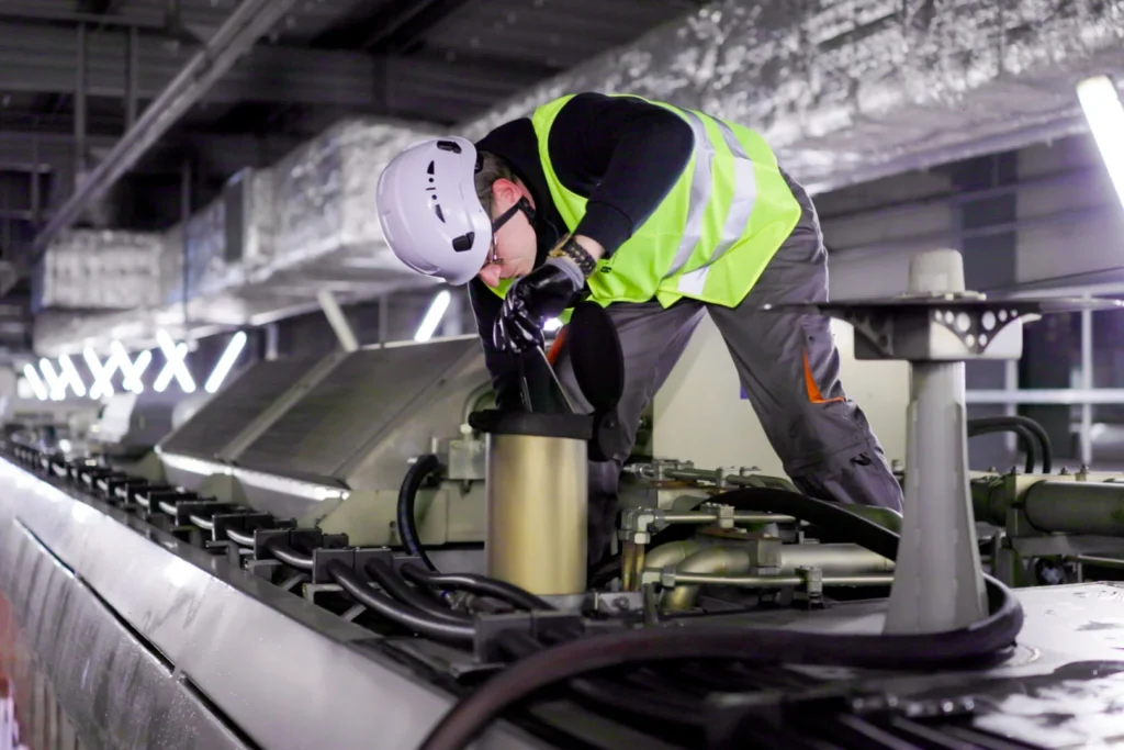 Un technicien portant un casque et un gilet de sécurité inspecte une installation industrielle complexe.