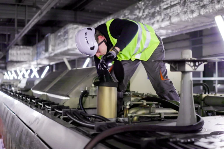 Un technicien portant un casque et un gilet de sécurité inspecte une installation industrielle complexe.