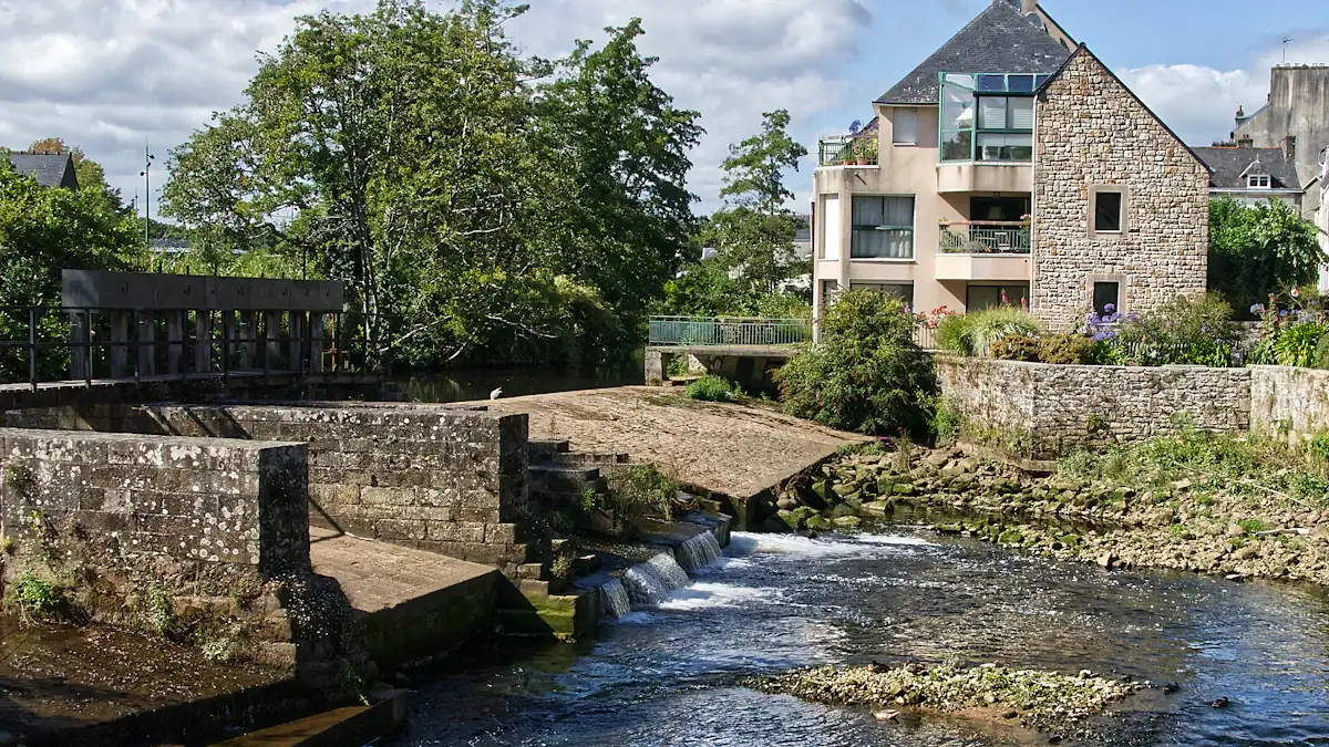 Vue paisible d'une rivière française avec une écluse et un bâtiment en pierre.