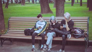 Trois adolescents assis sur un banc de bois dans un parc, occupés avec leurs téléphones portables.