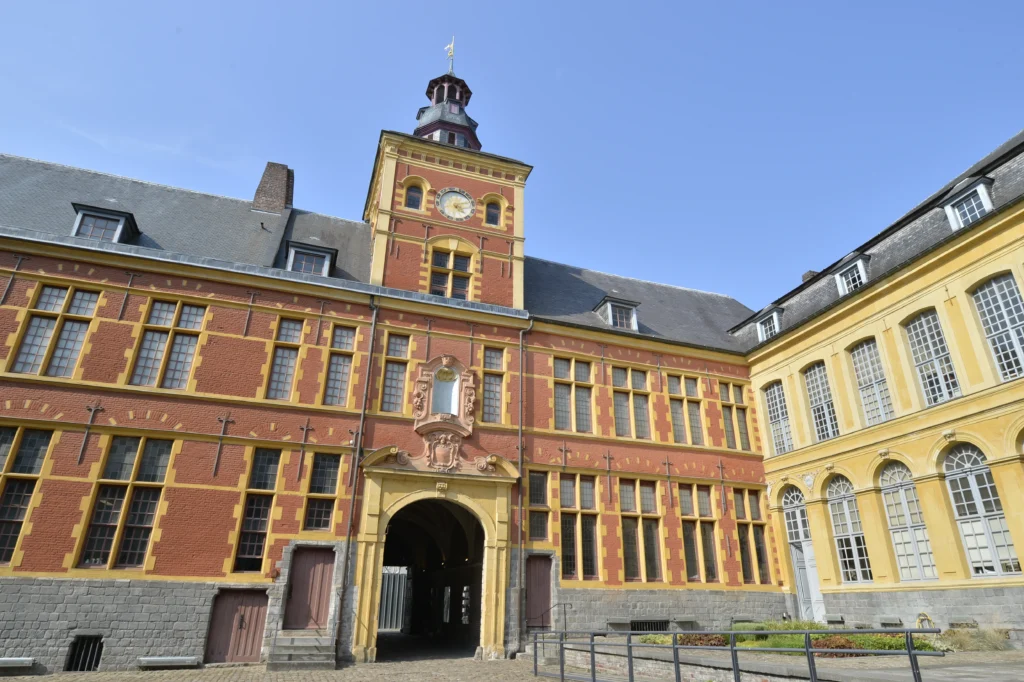 Bâtiment en briques rouges et pierres jaunes avec tour d'horloge et grand porche central.