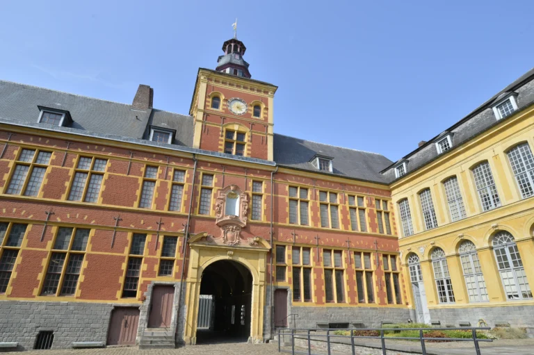 Bâtiment en briques rouges et pierres jaunes avec tour d'horloge et grand porche central.