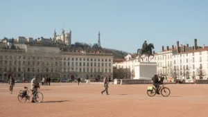 Vue panoramique de la place Bellecour à Lyon montrant des piétons et des cyclistes en journée.