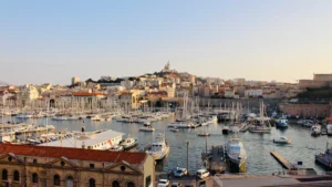 Vue panoramique sur le Vieux-Port de Marseille avec la basilique Notre-Dame de la Garde en arrière-plan sous une lumière de fin de journée.