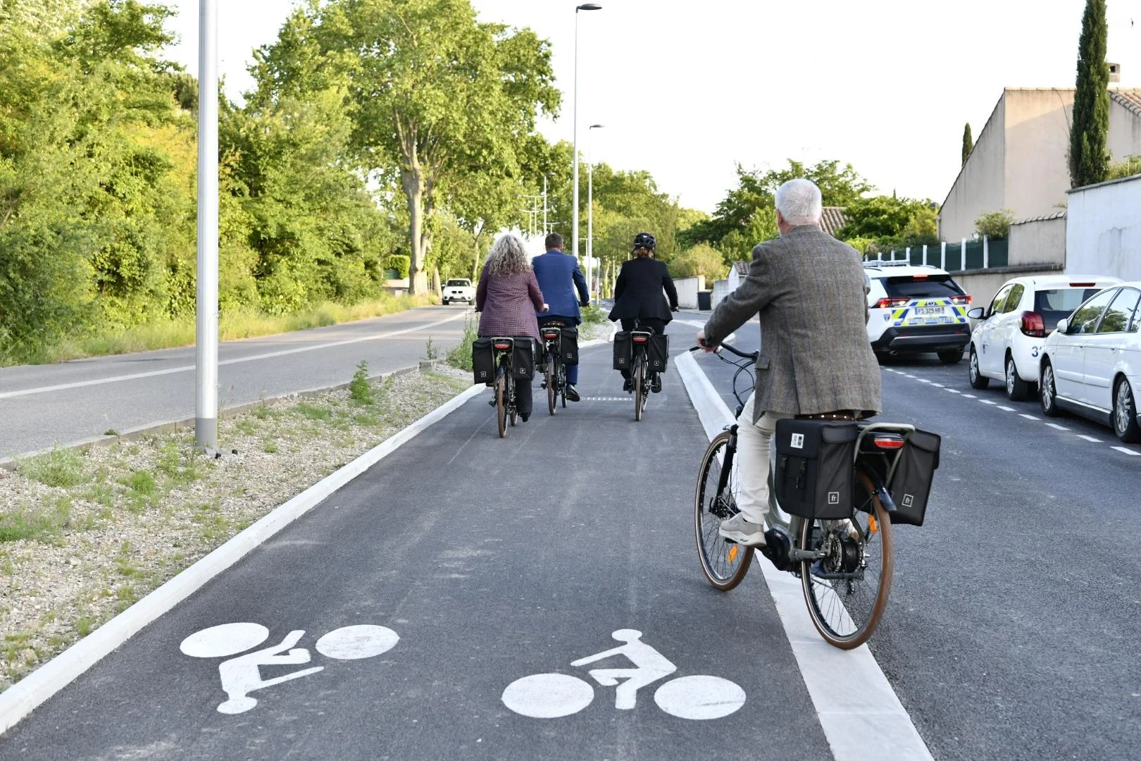 Quatre cyclistes avec sacoches circulent sur une piste cyclable sécurisée marquée de symboles blancs.