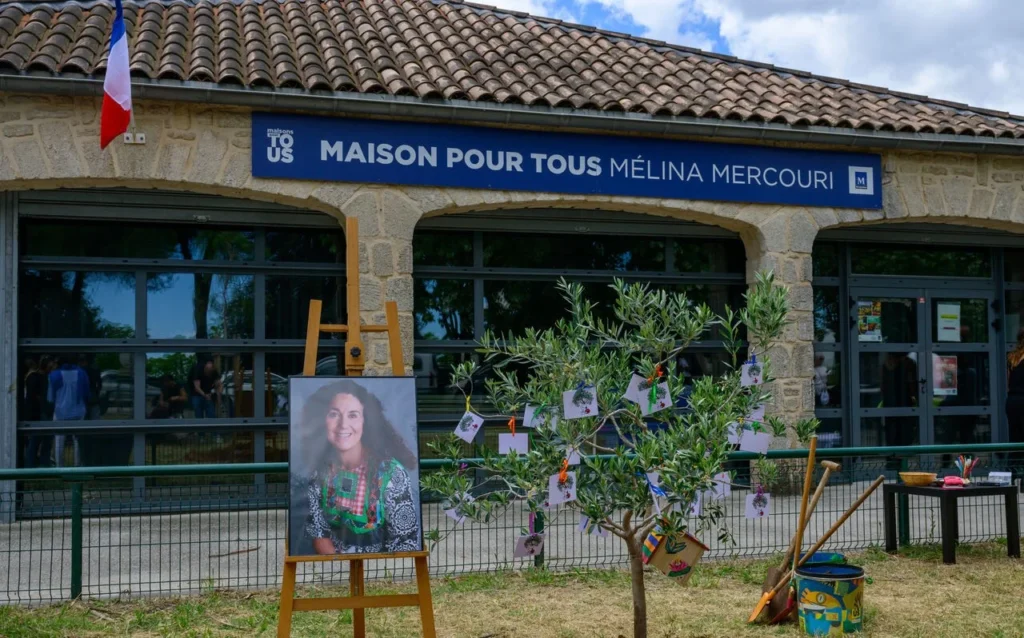Portrait de femme sur chevalet devant la Maison pour tous Mélina Mercouri et un petit olivier.