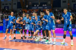 Équipe de volleyball masculine en maillot bleu posant sur un terrain lors d'un match intérieur.