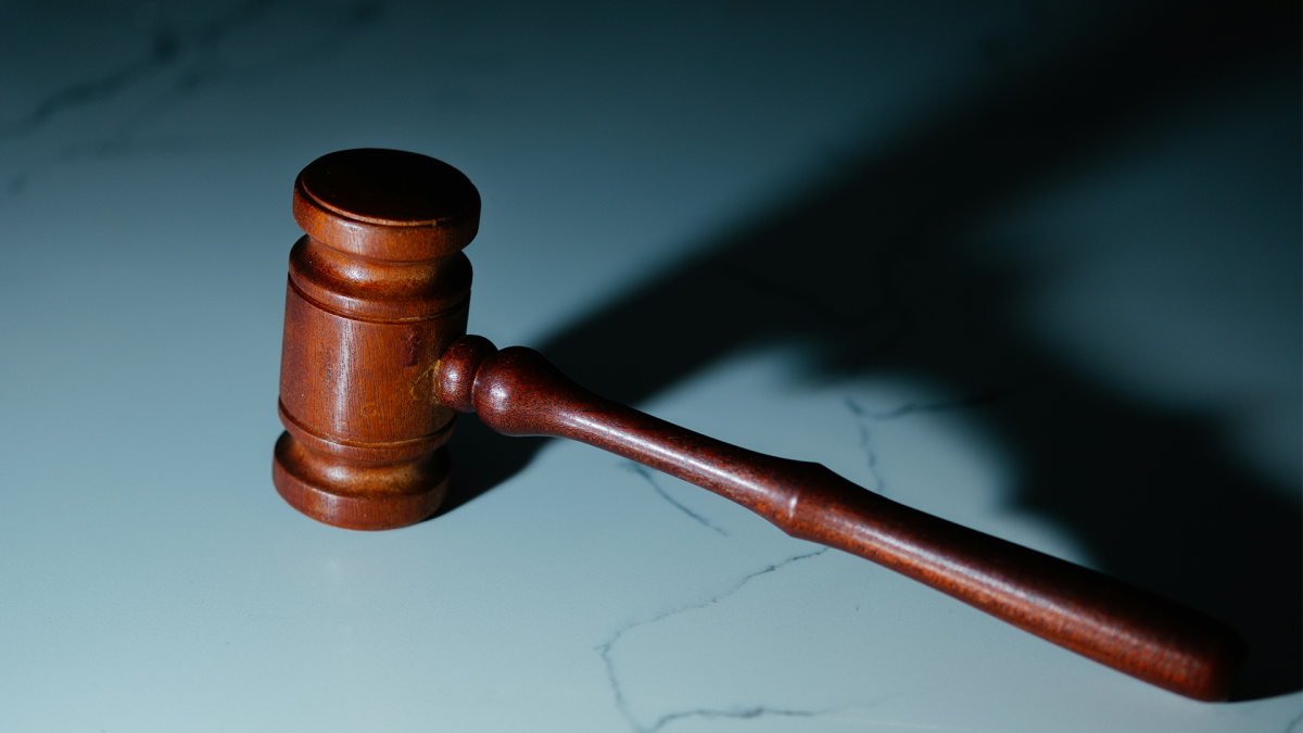 Marteau de justice en bois posé sur une surface claire avec une ombre portée allongée.