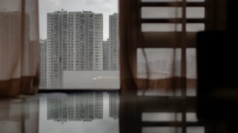 Une vue urbaine de grands immeubles modernes à travers les rideaux d'une fenêtre en intérieur.