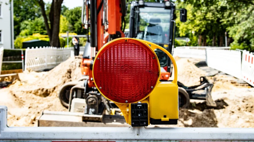 Gros plan d'un feu de signalisation de chantier rouge devant une pelleteuse en zone urbaine.
