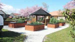 Un jardin communautaire avec des bacs de potager en bois et un kiosque central sous un ciel bleu à Nanterre.