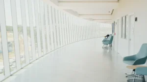 Un long couloir moderne et lumineux d'un hôpital avec des chaises design et de grandes baies vitrées.