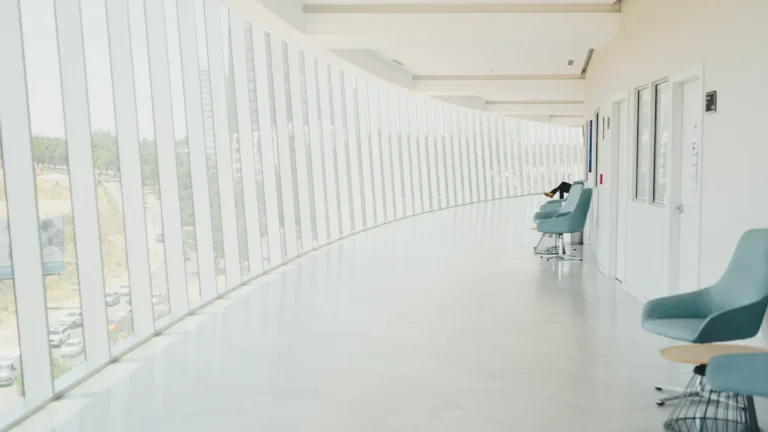 Un long couloir moderne et lumineux d'un hôpital avec des chaises design et de grandes baies vitrées.