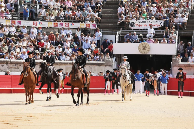 Trois cavaliers en tenue traditionnelle défilent à cheval dans une arène devant un public nombreux.