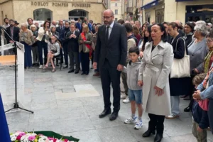 Un homme, un enfant et une femme debout solennellement devant une foule et des fleurs.