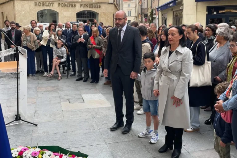 Un homme, un enfant et une femme debout solennellement devant une foule et des fleurs.