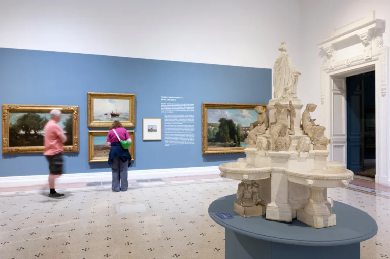 Galerie d'art avec des tableaux de paysages et une grande sculpture fontaine au premier plan.