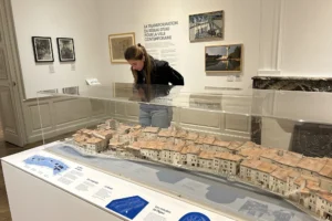 Une femme observe une maquette miniature d'un quartier historique exposée dans une galerie de musée.