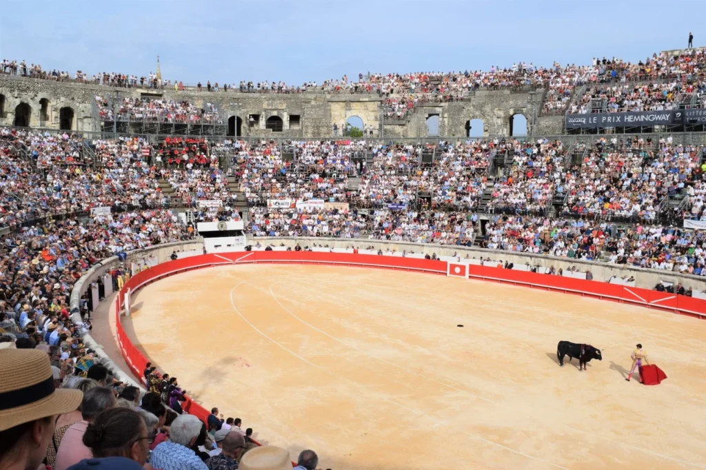 Matador avec cape rouge face à un taureau noir dans une arène bondée de spectateurs.
