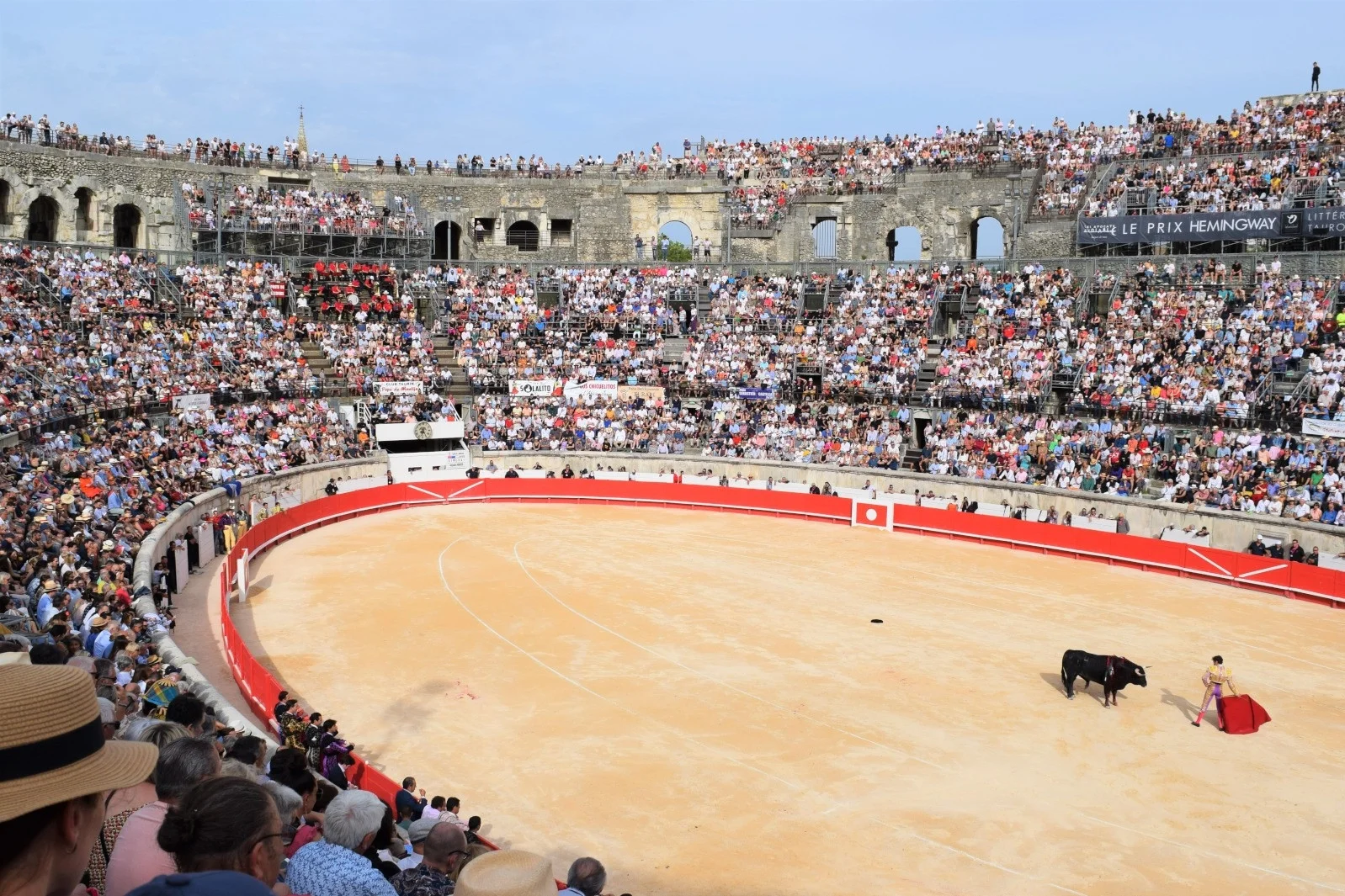 Matador avec cape rouge face à un taureau noir dans une arène bondée de spectateurs.