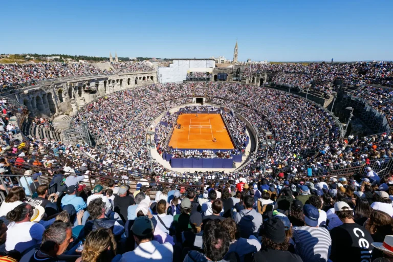 Vue aérienne d'un court de tennis en terre battue dans un amphithéâtre romain bondé de spectateurs.