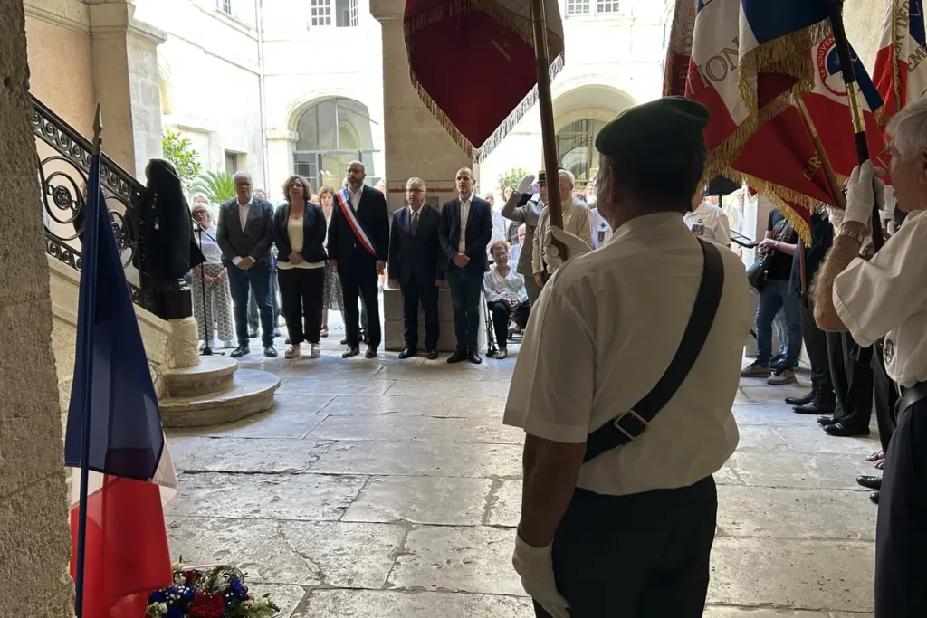 Un groupe de personnes assiste à une cérémonie officielle avec des drapeaux français officiels.