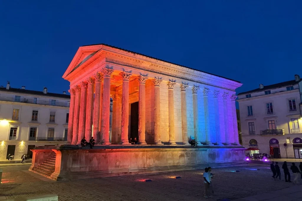 Temple romain antique de Nîmes illuminé aux couleurs du drapeau français pendant la nuit.