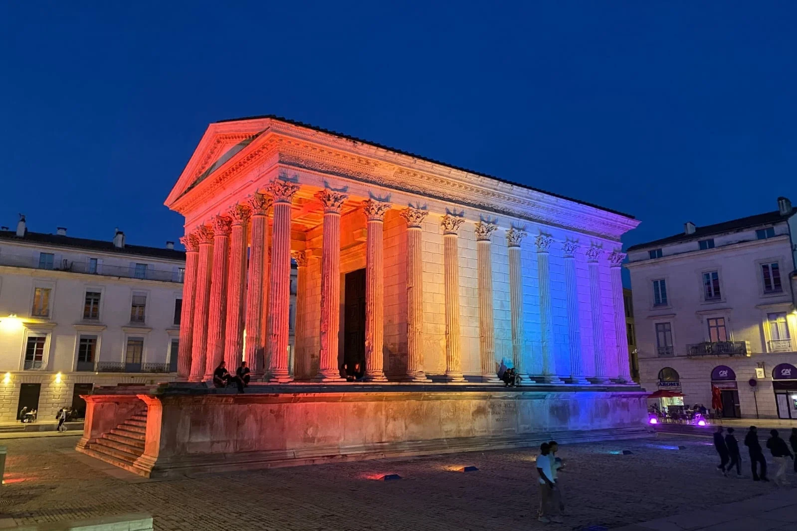 Temple romain antique de Nîmes illuminé aux couleurs du drapeau français pendant la nuit.