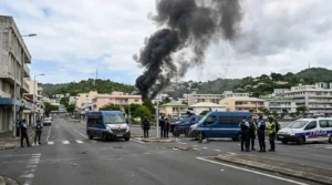 Gendarmes et policiers surveillent une épaisse colonne de fumée noire s'élevant d'une zone urbaine.
