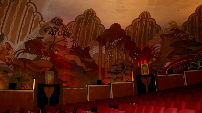 Intérieur orné d'un théâtre classique avec des fresques murales et des fauteuils en velours rouge.