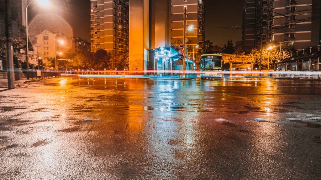 Chaussée détrempée et reflets de lumières urbaines dans une rue de ville la nuit après un orage.
