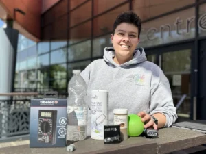 Une personne souriante présente du vinaigre, du sel et un multimètre posés sur une table extérieure.