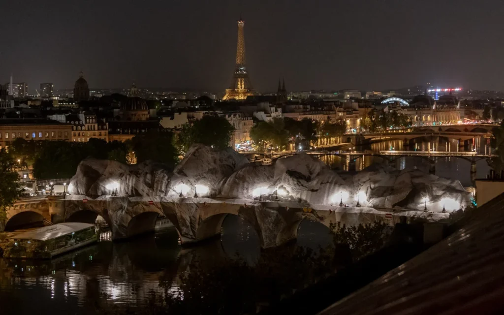 Pont-Neuf de Paris emballé de tissu clair illuminé de nuit avec la Tour Eiffel lointaine.
