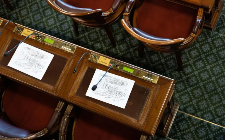 Vue en plongée de bureaux en bois avec microphones et documents du Conseil de Paris.
