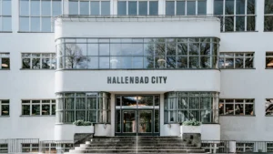 Façade blanche d'une piscine municipale urbaine avec de larges baies vitrées et escaliers.