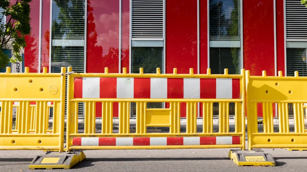 Barrières de chantier jaunes et rouges installées devant la façade moderne d'un bâtiment en ville.