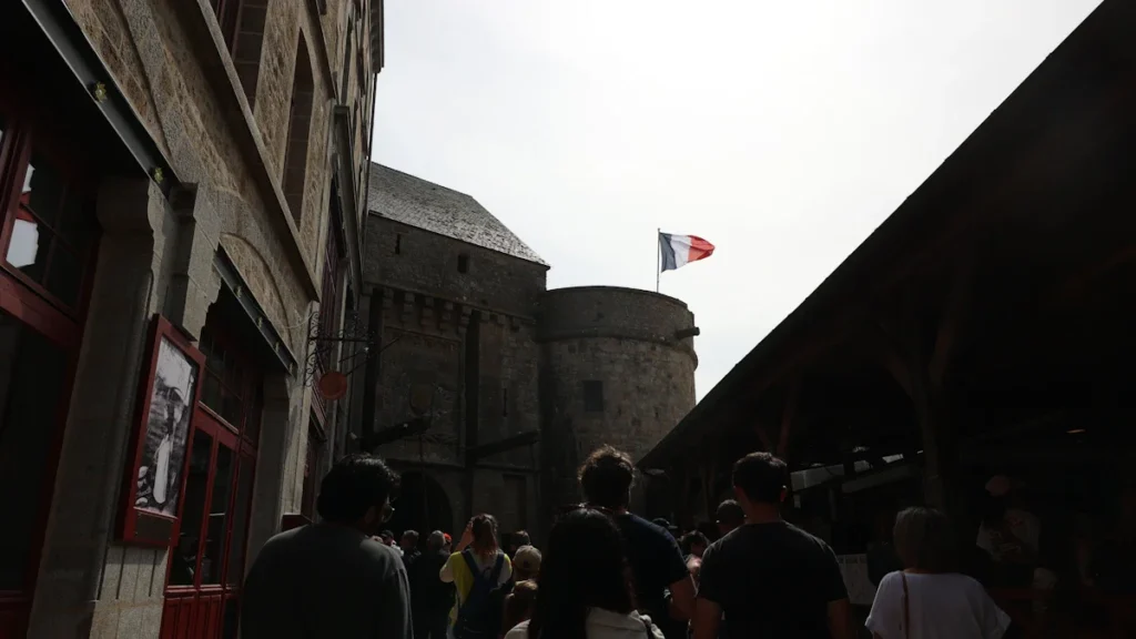 Des visiteurs marchant vers un monument historique français pavoisé d'un drapeau bleu-blanc-rouge.