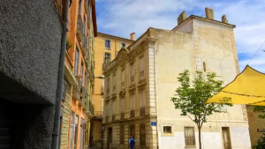 Une ruelle ensoleillée de Perpignan avec des bâtiments historiques aux façades colorées typiques.