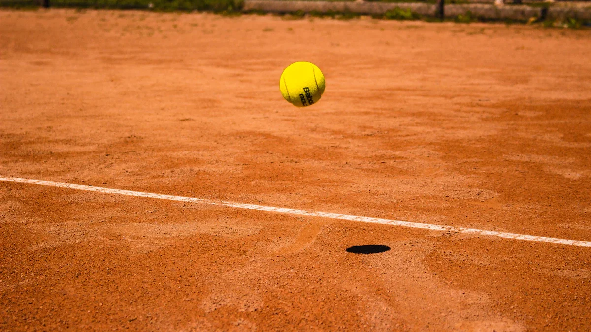 Une balle de tennis jaune en plein rebond sur un court de terre battue ocre ensoleillé.