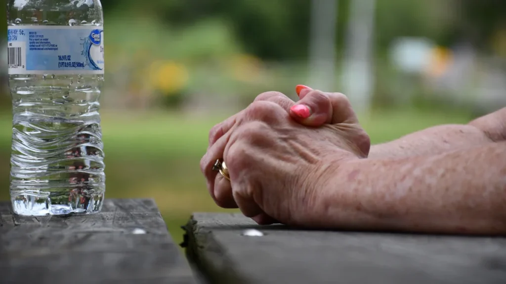 Mains d'une personne âgée posées sur une table à côté d'une bouteille d'eau par forte chaleur.