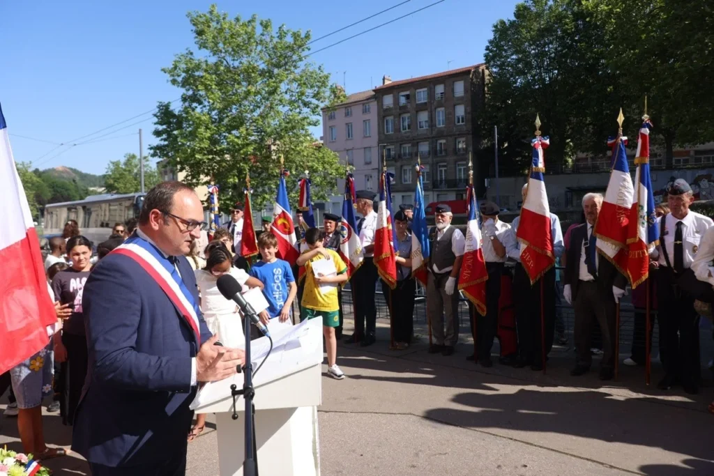 Un maire prononce un discours lors d'une cérémonie commémorative officielle avec de nombreux drapeaux français.